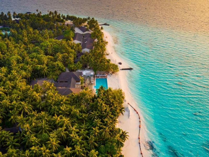Aerial view of a resort with beach, lush palm trees, and blue sea at sunset.