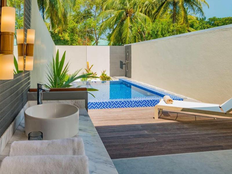 Modern outdoor area with pool, lounge chair, and seating in tropical hotel.