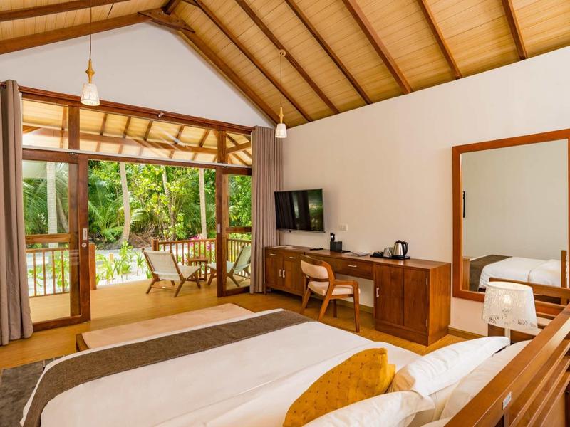 Cozy hotel room with wooden beam ceiling, large bed, and access to veranda with garden view.