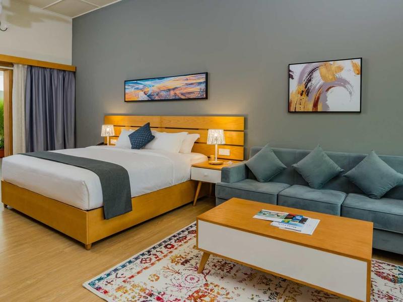 Modern hotel room with double bed, sofa, and cozy lighting.