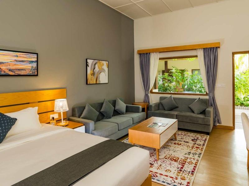 Modern hotel room with large bed, seating area, and garden view through window.