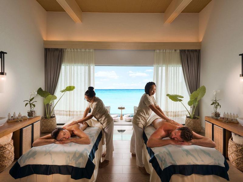 Couple profitant d'un massage en duo dans un spa luxueux avec vue sur la mer et lumière naturelle.