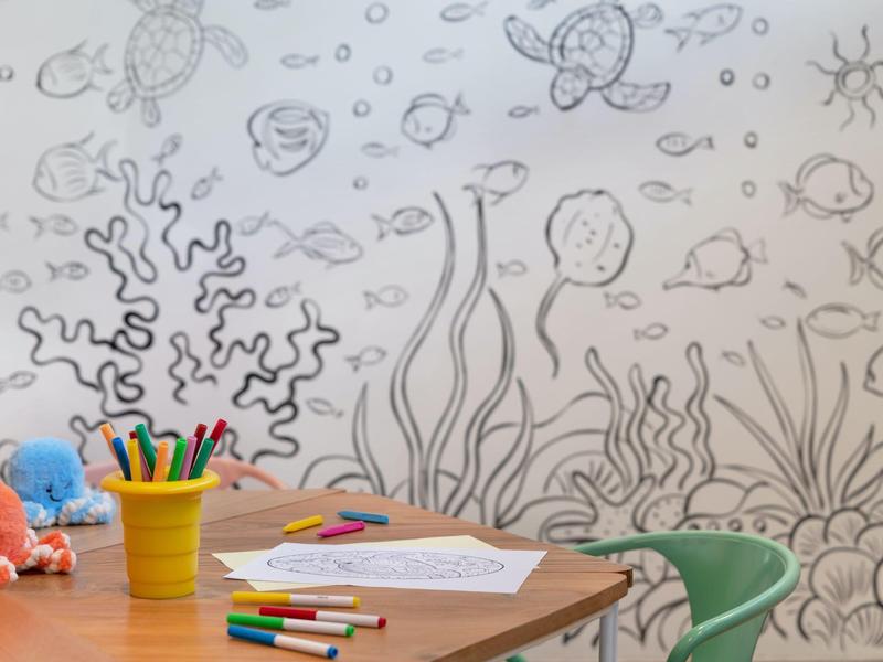 Table d'enfant avec crayons de couleur et papier devant un coloriage mural sur le thème sous-marin