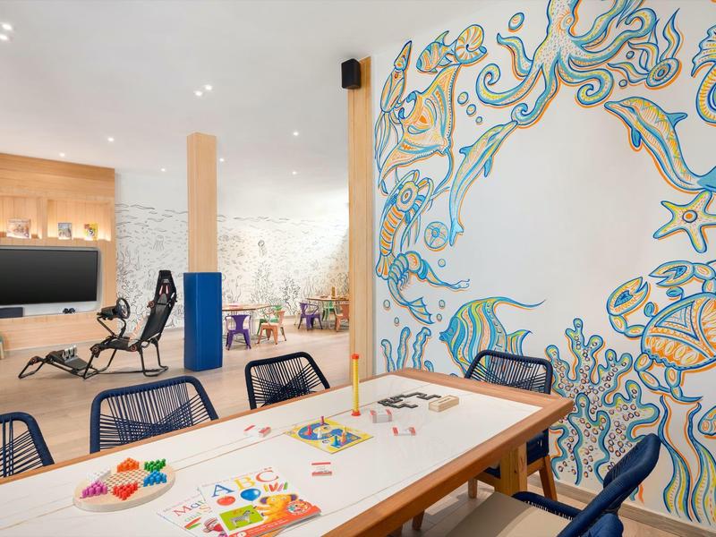 Salle moderne avec une longue table, plusieurs chaises et une fresque murale marine colorée.