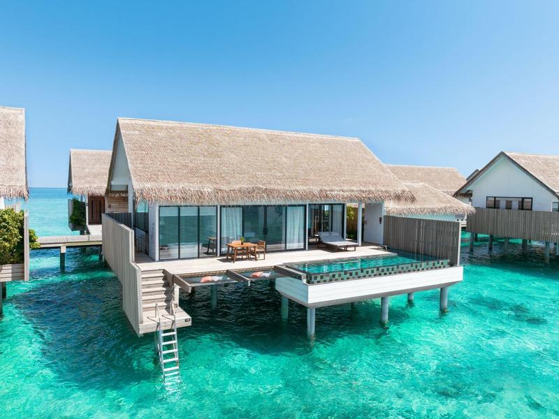 Bungalow sur pilotis avec terrasse et piscine privée sur l'eau turquoise sous un ciel clair.