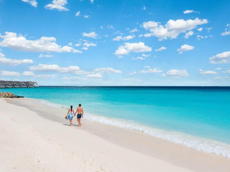 Couple marchant sur une plage de sable blanc avec eau turquoise claire et ciel bleu.
