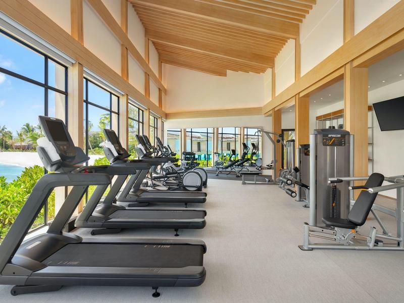 Salle de sport lumineuse avec tapis de course et machines de fitness donnant sur la piscine et le jardin.