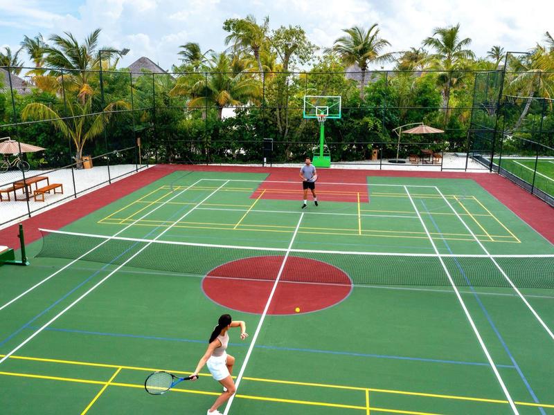 Terrain de basketball extérieur avec des joueurs entouré de palmiers dans une station tropicale.