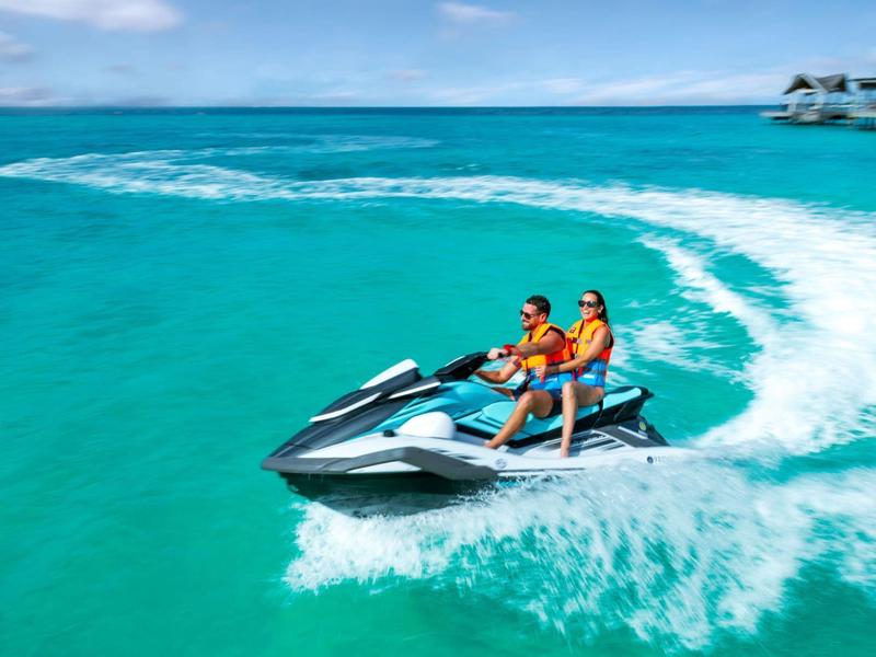 Deux personnes font du jet ski sur une mer turquoise près de villas sur l'eau.
