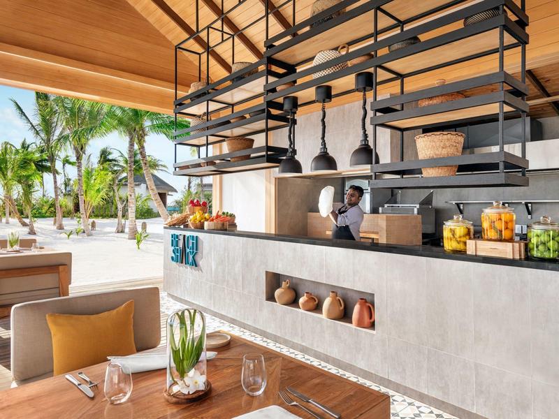 Espace de restaurant extérieur moderne avec bar, tabourets et vue sur des plantes tropicales.
