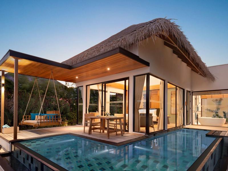 Maison moderne avec coin salon couvert et piscine au coucher du soleil.