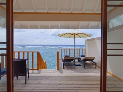 Vue depuis une chambre sur une terrasse avec chaises longues et parasol au bord de la mer