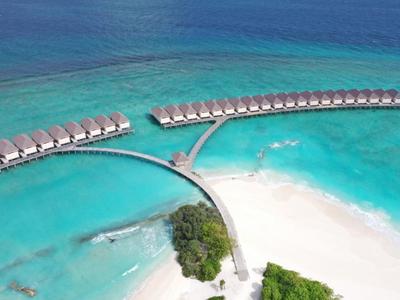 Vue aérienne de bungalows sur pilotis au-dessus de la mer turquoise avec plages de sable blanc.
