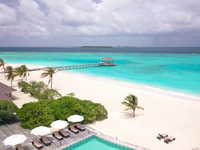 Station balnéaire avec plages de sable blanc, eau turquoise et palmiers sous un ciel nuageux.