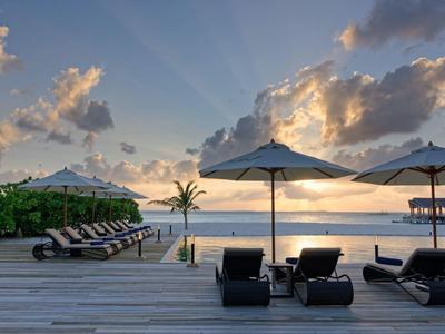 Coucher de soleil sur une plage tropicale avec des chaises longues et des parasols sur une terrasse en bois.