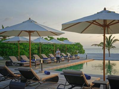 Espace piscine avec chaises longues et parasols au bord de la mer au coucher du soleil