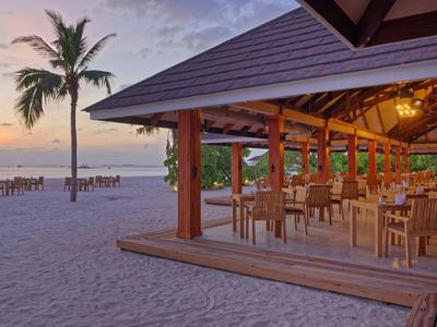 Restaurant de plage ouvert avec des tables en bois et des palmiers au coucher du soleil.