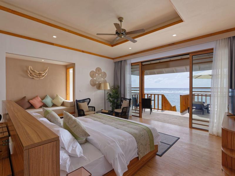 Chambre d'hôtel lumineuse et moderne avec deux lits, coin salon et vue sur terrasse avec piscine et jardin.