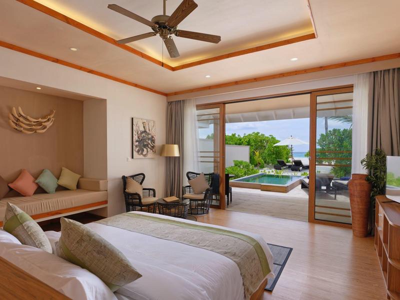 Chambre d'hôtel lumineuse et moderne avec deux lits, coin salon et vue sur terrasse avec piscine et jardin.