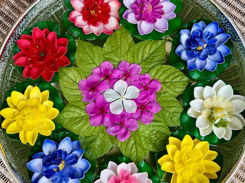 Bougies en forme de fleurs colorées disposées sur un plateau rond avec des feuilles vertes.