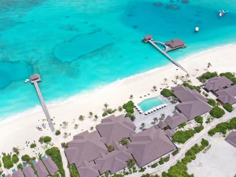 Vue aérienne d'un complexe tropical avec bungalows en bord de plage et jetées sur l'eau turquoise.