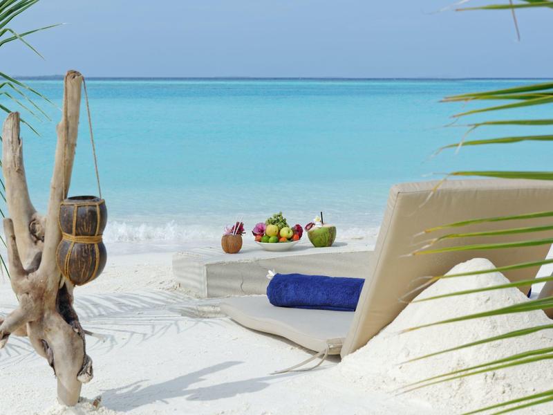 Chaises longues sur le sable avec plateau de fruits devant mer turquoise et ciel clair