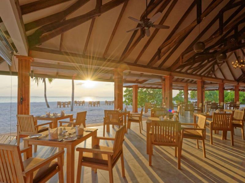 Restaurant en plein air avec mobilier en bois et vue sur la mer au coucher du soleil.