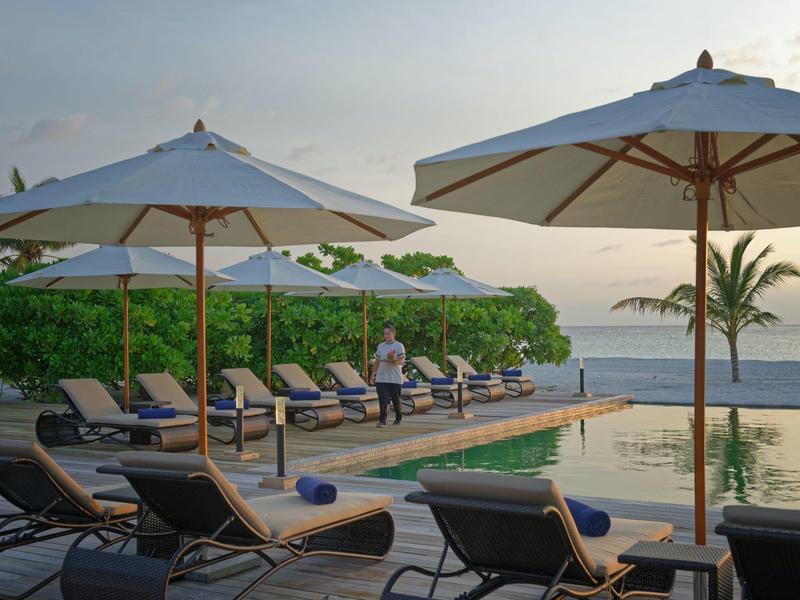 Espace piscine avec chaises longues et parasols au bord de la mer au coucher du soleil