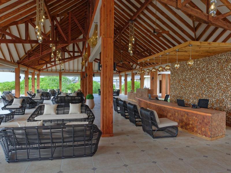 Espace lounge ouvert avec plafond en bois, mur en pierre et sièges modernes dans un hôtel.