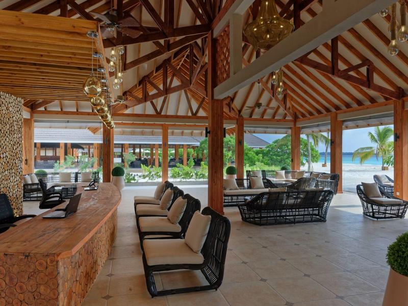 Espace lounge ouvert avec sièges et bar dans un cadre hôtelier tropical.