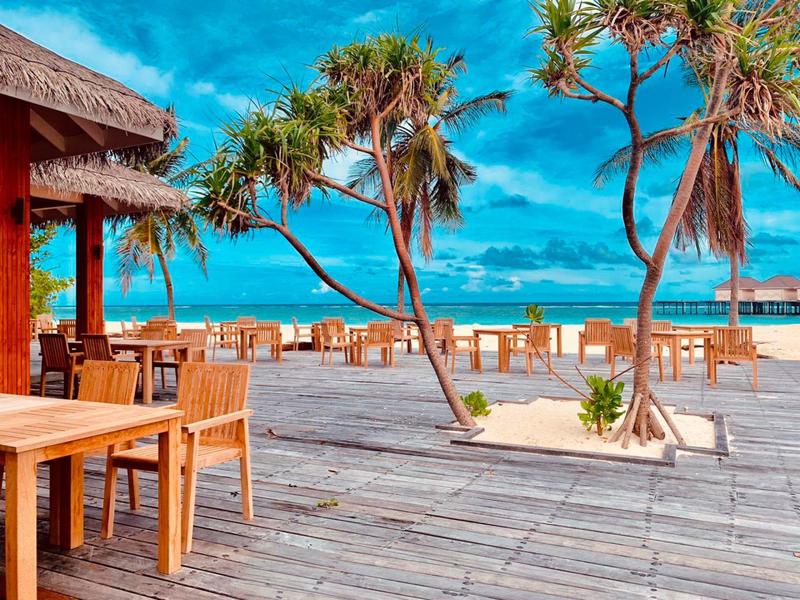 Pavillon en bois et terrasse avec chaises sur la plage sous un ciel bleu.