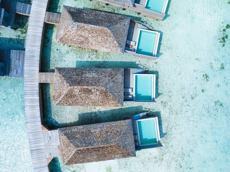 Vue aérienne de cabanes de plage avec toits de chaume et chaises longues bleues sur la plage de sable.