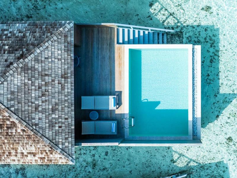 Vue aérienne d'une piscine moderne à côté d'une terrasse en bois avec des chaises longues dans un hôtel.