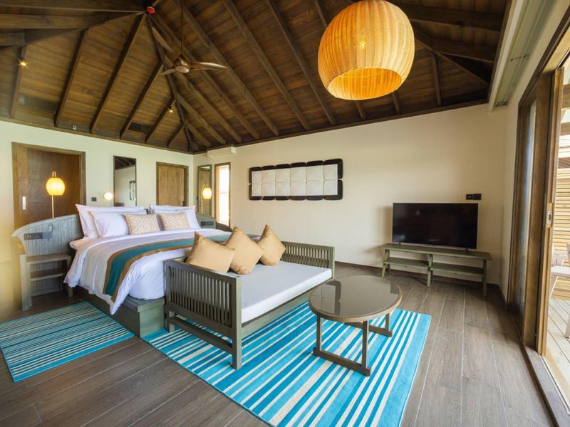 Chambre d'hôtel confortable avec sol en bois, lit à baldaquin, canapé et grande fenêtre donnant sur l'extérieur.