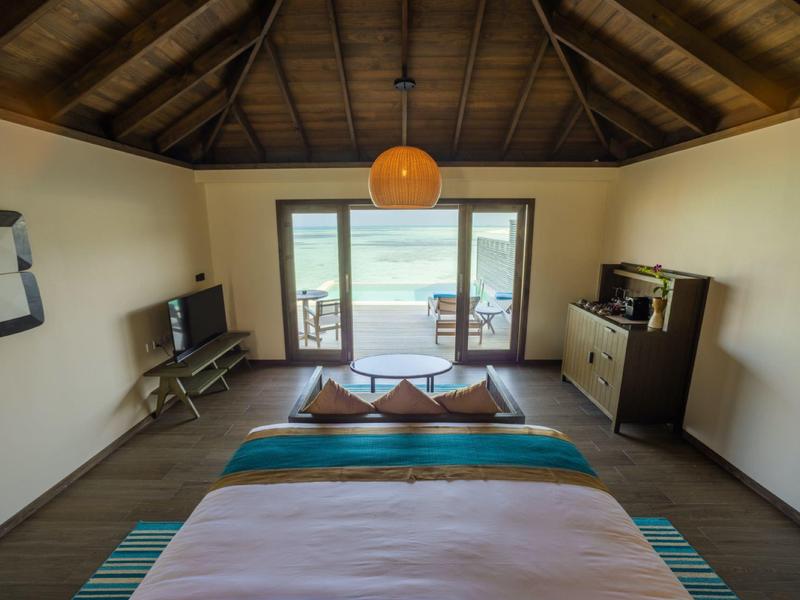 Chambre d'hôtel moderne avec plafond en bois, lit double et vue sur la mer à travers de grandes fenêtres.