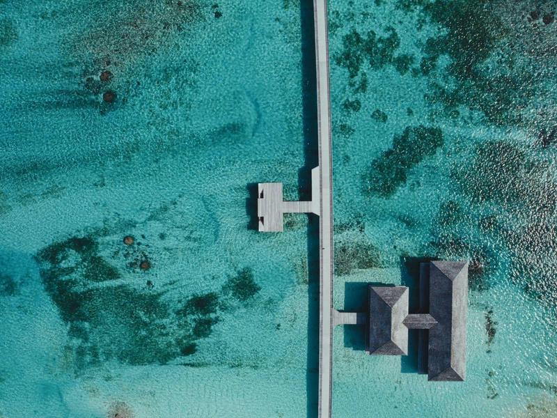 Vue aérienne d'une jetée et d'un bungalow au-dessus d'une eau de mer turquoise claire.