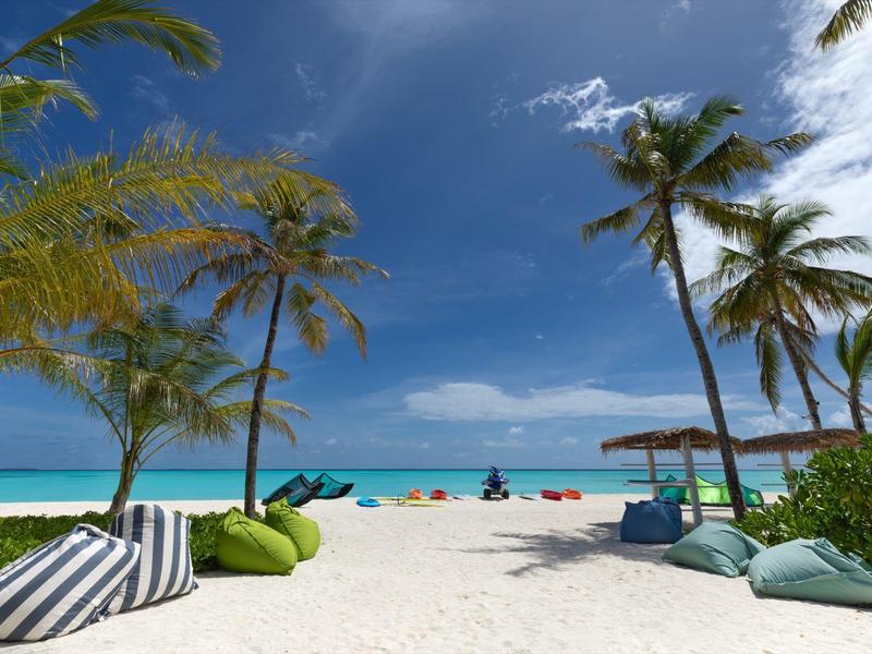 Pláž s bílým pískem, palmami, křesly a výhledem na modré moře pod zataženou oblohou.
