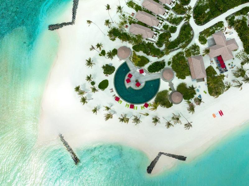 Letecký pohled na tropický resort s bílou písečnou pláží a čistou tyrkysovou vodou.