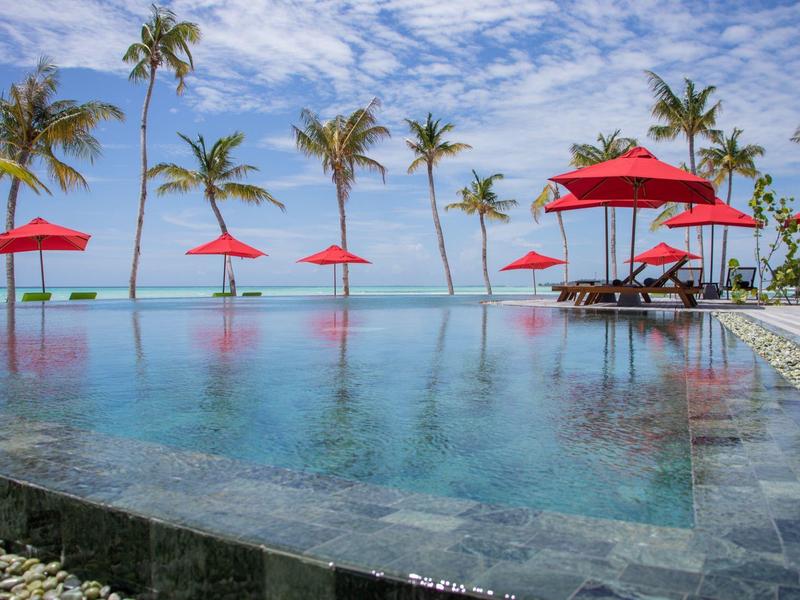 Infinity bazén s červenými slunečníky a palmami na pozadí modré oblohy a moře