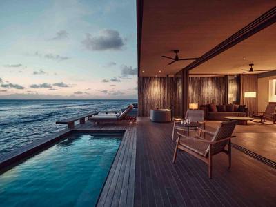 Modern beach bungalow with wooden deck, infinity pool, and ocean view at sunset.