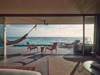 Modern outdoor area with hammock, chairs, and sea view at sunset