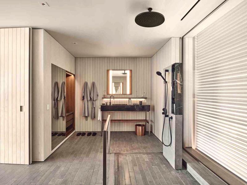 Modern bathroom with illuminated mirror, rain shower, and wooden accents.