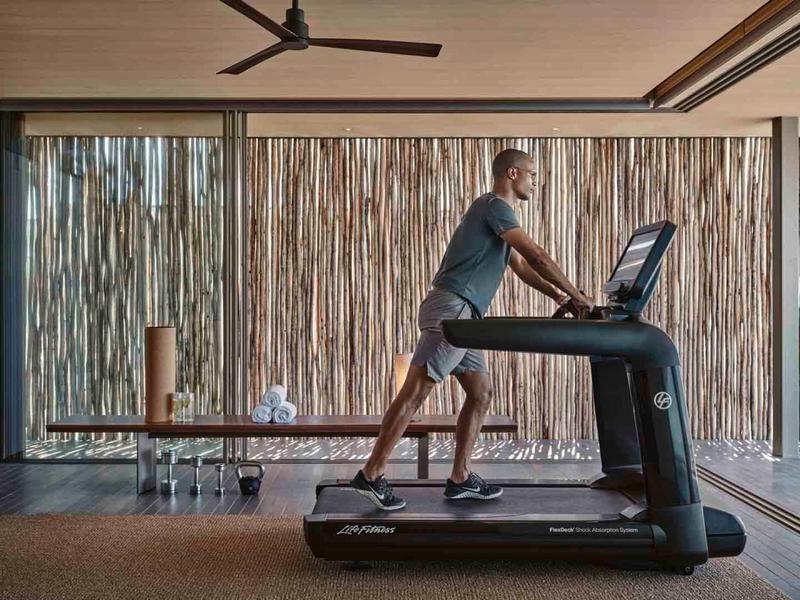 Man exercising on treadmill in stylish gym with natural wooden backdrop.