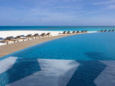 Large pool with lounge chairs next to a white sandy beach and blue sea in the background.