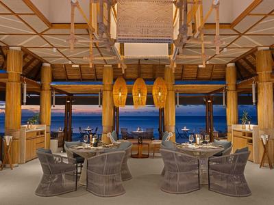 Open restaurant area with stylish seating, wooden columns, and a sea view at dusk.
