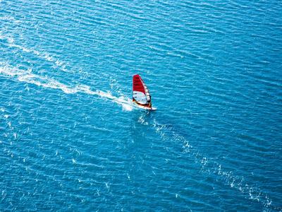 Windsurfař s červenou plachtou klouže po modré vodě.