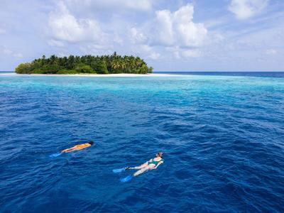 Two snorkelers swim in clear blue water with a tropical island in the background.