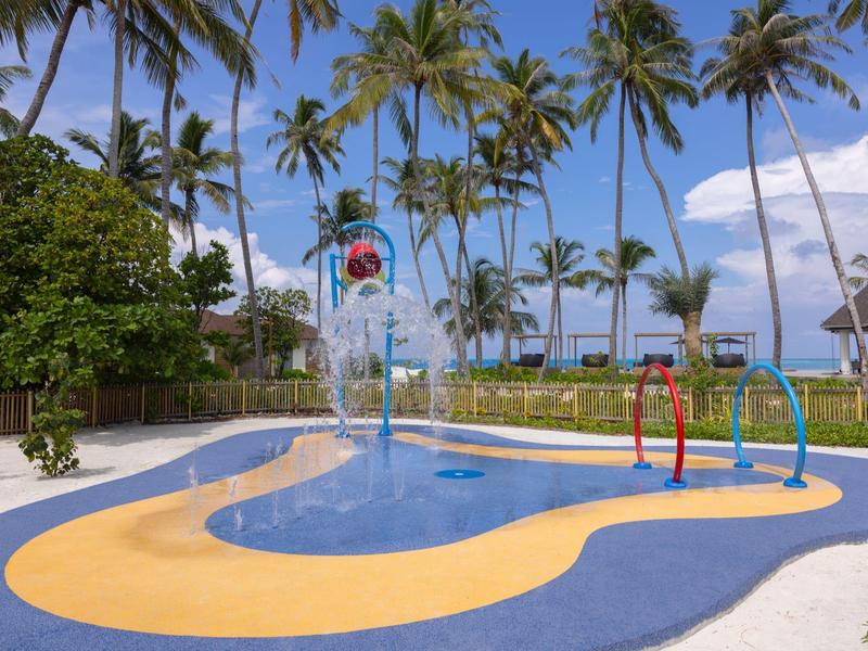 Small colorful children's splash pool with water features under palm trees by the beach.