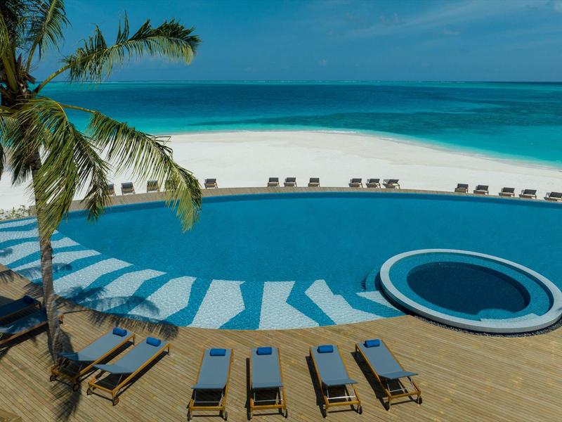 Several lounge chairs and a pool overlooking a white sandy beach and blue sea.