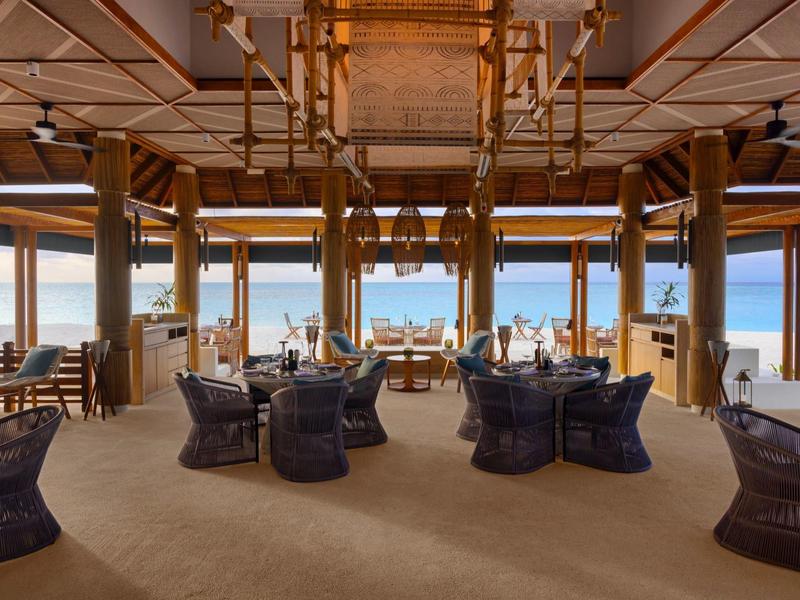 An open wooden-paneled dining area with sea view and outdoor seating groups.